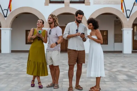Viajeros explorando durante un tour gastronómico autoguiado, usando sus teléfonos para navegar entre restaurantes locales y lugares de comida escondidos en las Islas Baleares.