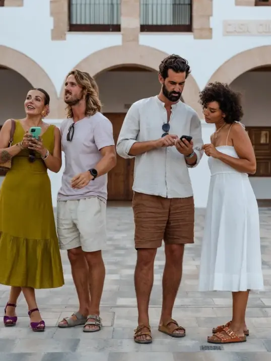 Viajeros explorando durante un tour gastronómico autoguiado, usando sus teléfonos para navegar entre restaurantes locales y lugares de comida escondidos en las Islas Baleares.