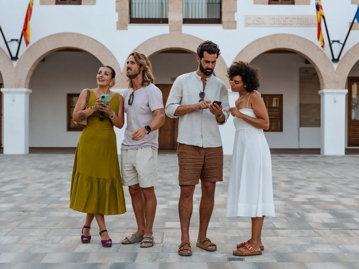 Viajeros explorando durante un tour gastronómico autoguiado, usando sus teléfonos para navegar entre restaurantes locales y lugares de comida escondidos en las Islas Baleares.