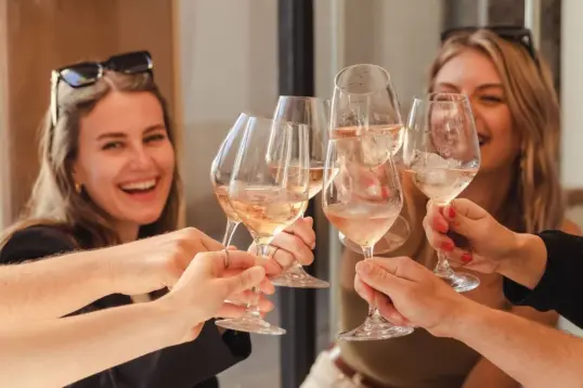 Amigas brindando con copas de vino rosado en un restaurante.