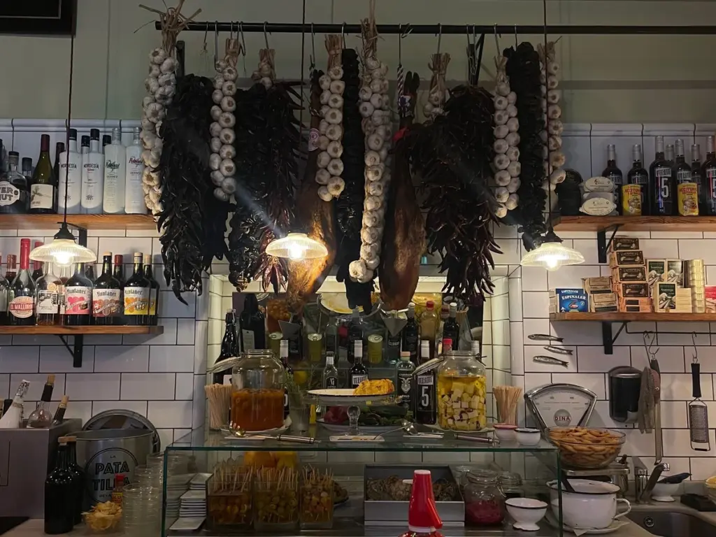 Interior de una vermutería tradicional en Palma de Mallorca con embutidos colgados, botellas de vermut y una barra clásica.